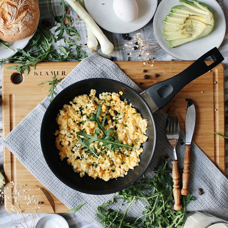 Profi Edelstahl-Bratpfanne 20cm with scrambled eggs and herbs on a wooden board.