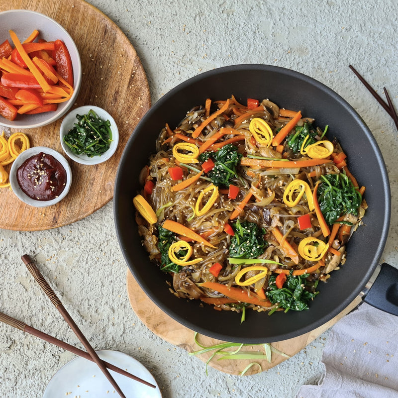 Profi Edelstahl-Wok 28cm filled with stir-fried vegetables, served with colorful ingredients on a wooden board.