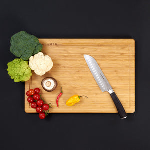 Santoku Damastmesser auf einem Schneidebrett mit frischem Gemüse und Kräutern für vielseitige Zubereitung.