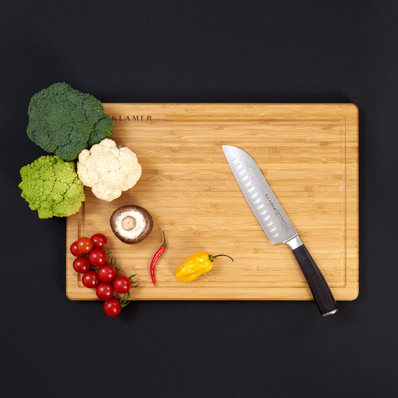 Santoku Damastmesser auf einem Schneidebrett mit frischem Gemüse und Kräutern für vielseitige Zubereitung.