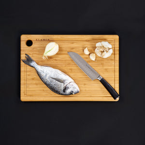 Santoku Damastmesser on a bamboo cutting board with fish, onion, and garlic.