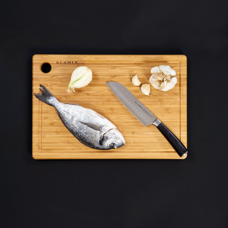 Santoku Damastmesser on a bamboo cutting board with fish, onion, and garlic.